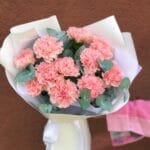 Bouquet of pink carnations with eucalyptus sprigs, wrapped in white paper and tied with a ribbon.