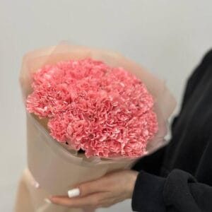 Pink carnation bouquet wrapped in light paper being held by a person in a black sleeve.